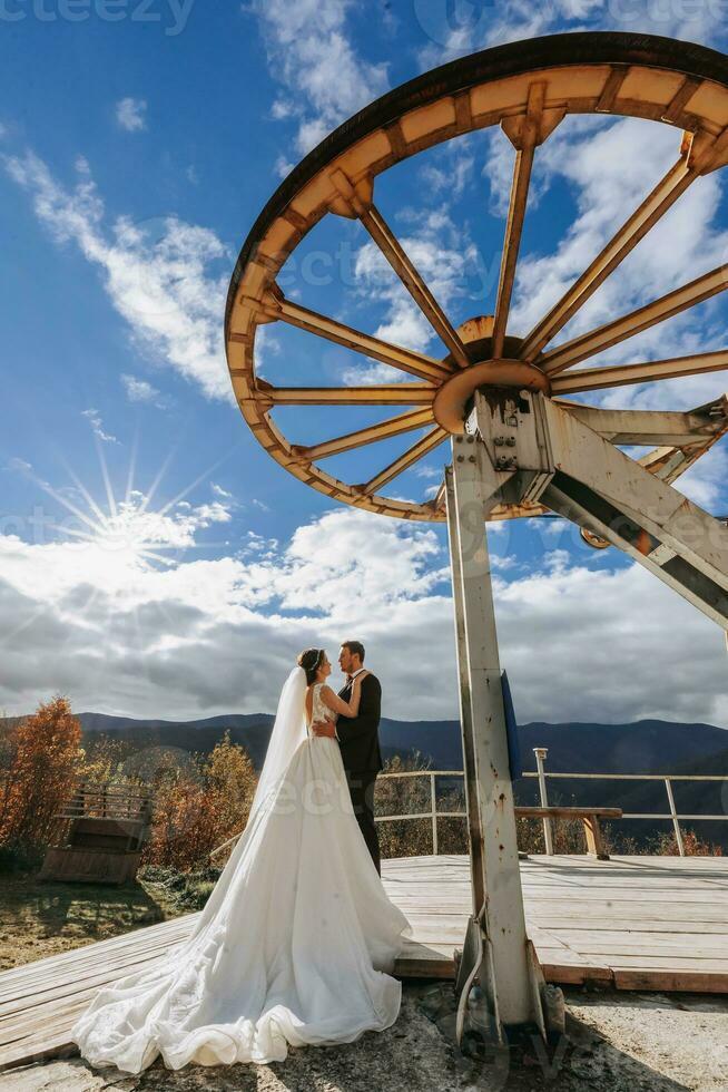 Married couple among mountains, bride looking at groom, hugging, girl smiling, woman in white wedding dress, groom and brown suit photo