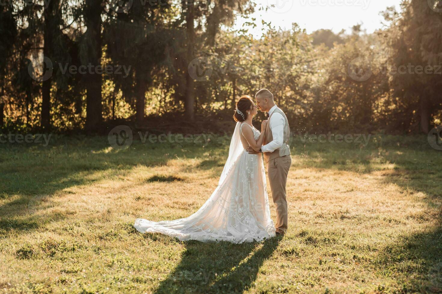 Wedding photo. The bride and groom are standing in a beautiful forest and beautiful light, hugging and leaning their noses against each other. Couple in love. Stylish groom photo