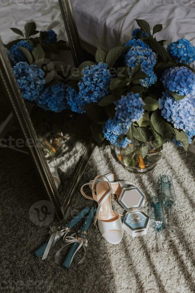 un Perfecto composición de el detalles de el novia. azul hortensias en el antecedentes de Boda anillos y de la novia zapatos. reflexión en el espejo. foto