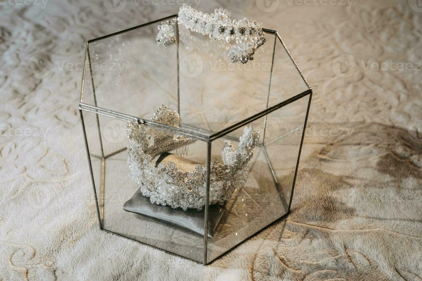Wedding crown tiara in a glass box on the bed, bracelet on the hand of the bride and royal earrings. Luxury accessories photo