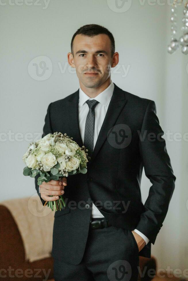 Portrait. A man in a white shirt, black bow tie and black tie poses in a room with a wedding bouquet. A stylish watch. Men's style. Fashion. Business photo