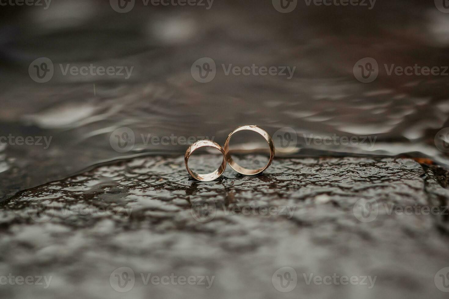 Wedding photography. Wedding rings stand on a stone in the water. Blurred background. Water. Wedding details. Brown background photo