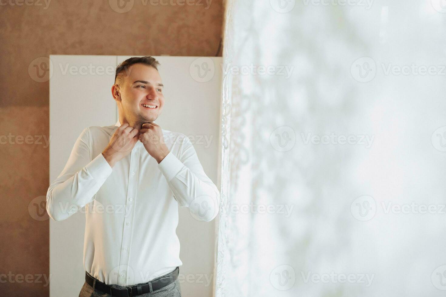 Portrait. A young stylish man in a white shirt poses looking to the side and fastens a button on his shirt. Fashion and style. business photo