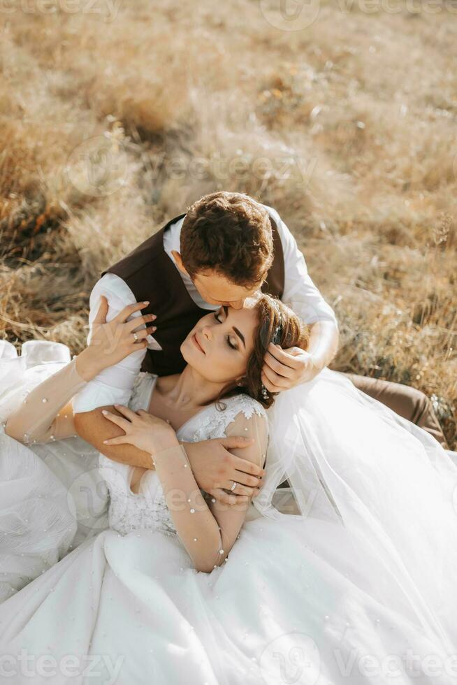 portrait of a stylish groom with a bride on a background of autumn dry grass. the concept of a rural wedding in the mountains, happy bohemian newlyweds. the bride and groom are lying on the grass photo