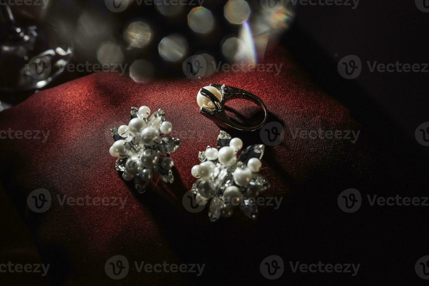 Silver bridal engagement ring with pearl and silver earrings with pearls on a red background. Beautiful light. Photo of wedding details.