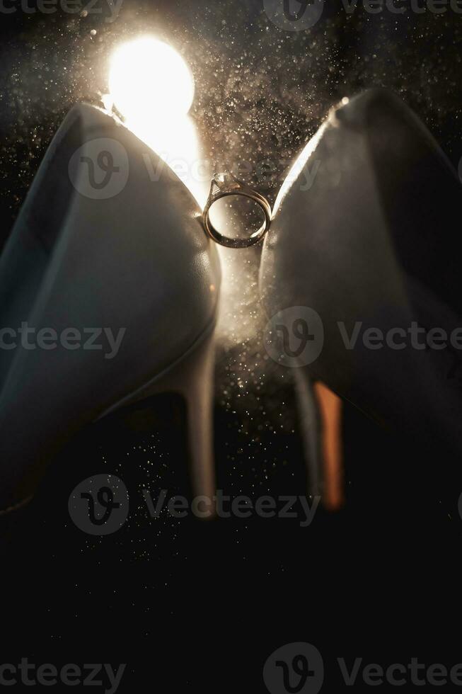 The bride's wedding ring stands on elegant white shoes in the backlight. Splashes of water on the shoes and wedding ring. Wedding photography photo