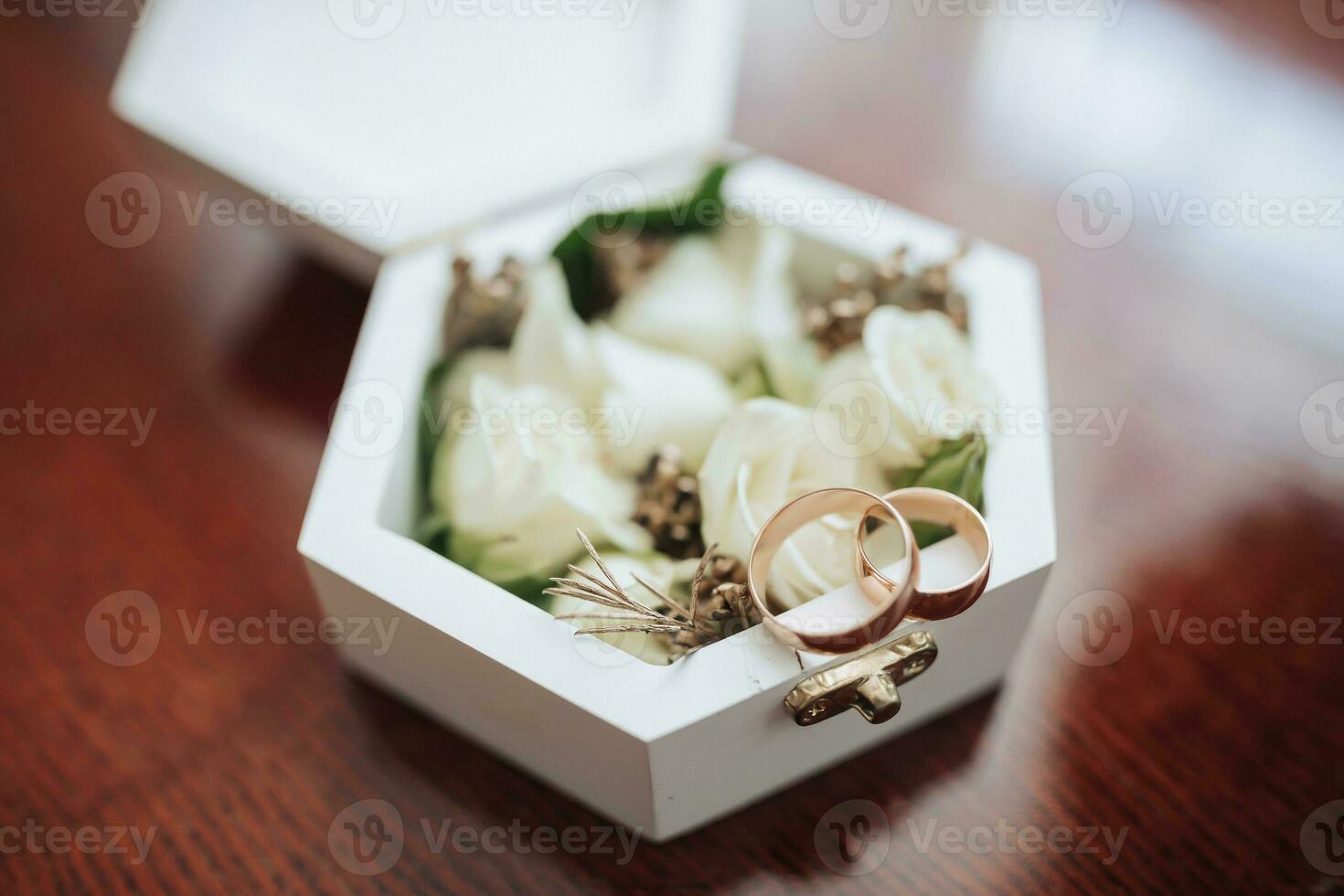 Photo of wedding accessories. Luxurious bouquet of the groom. Gold rings on a stand with flowers, white cufflinks on a wooden floor background.