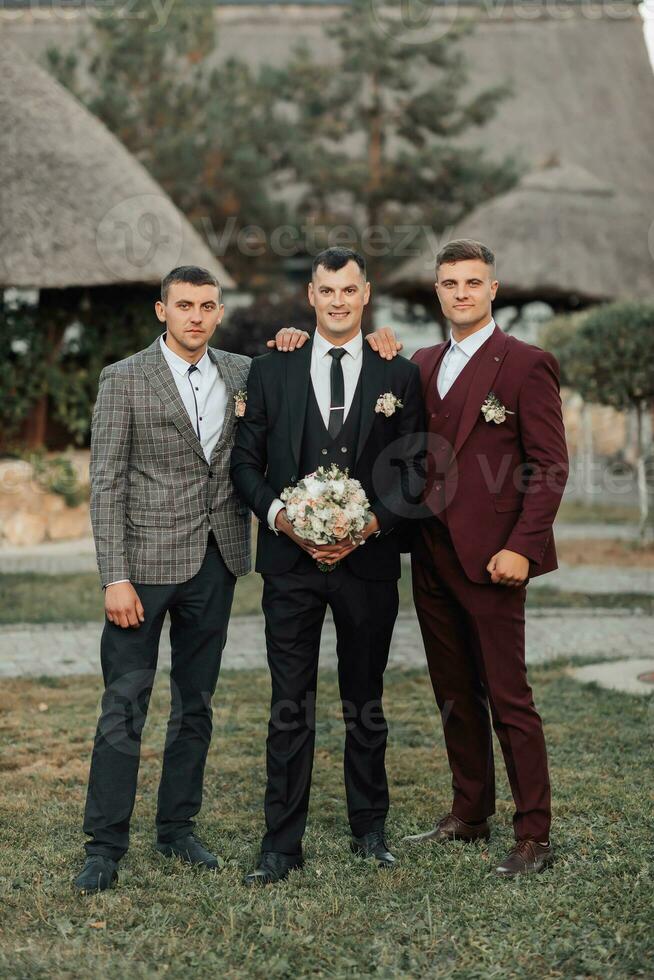 Photo of three men in classic suits. A man holds a bouquet while standing among his friends. Business style. Stylish men