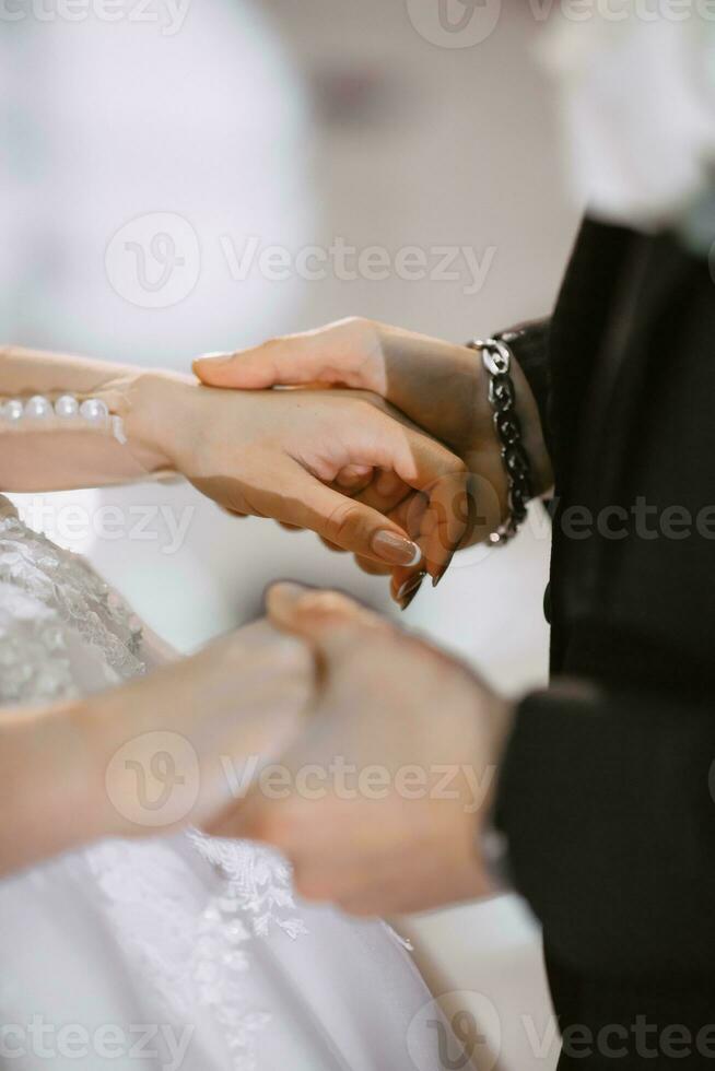 Handsome groom and charming bride stay together near modern wooden house in park. Close-up of the groom holding the bride's hand photo