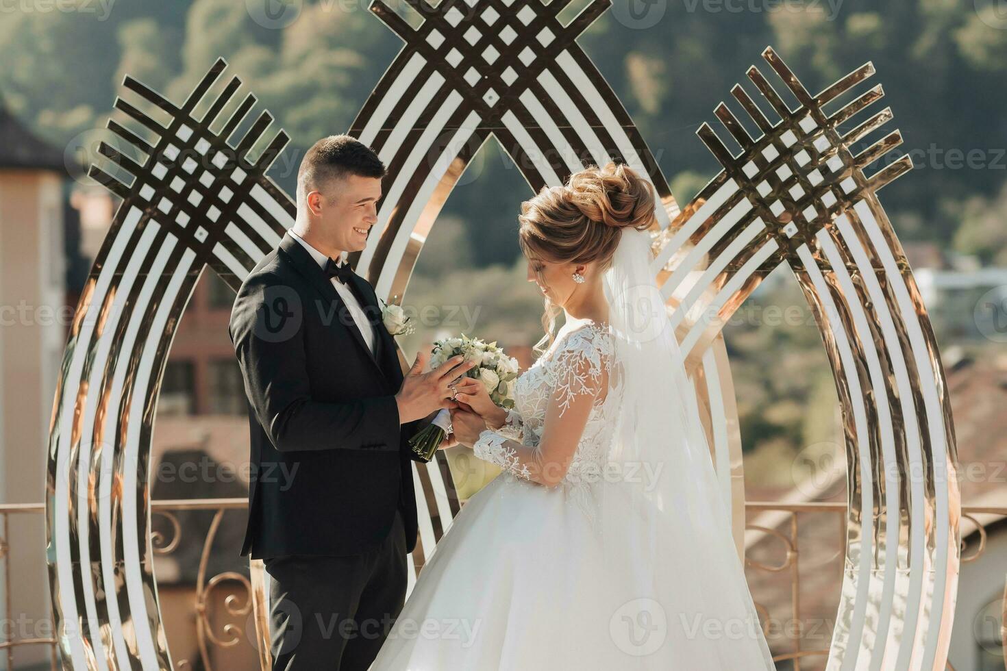 Wedding Portrait. Wedding ceremony painting in nature. The groom holds a bouquet and looks at the bride, the bride puts on the groom's wedding ring. Beautiful golden arch and fresh flowers photo
