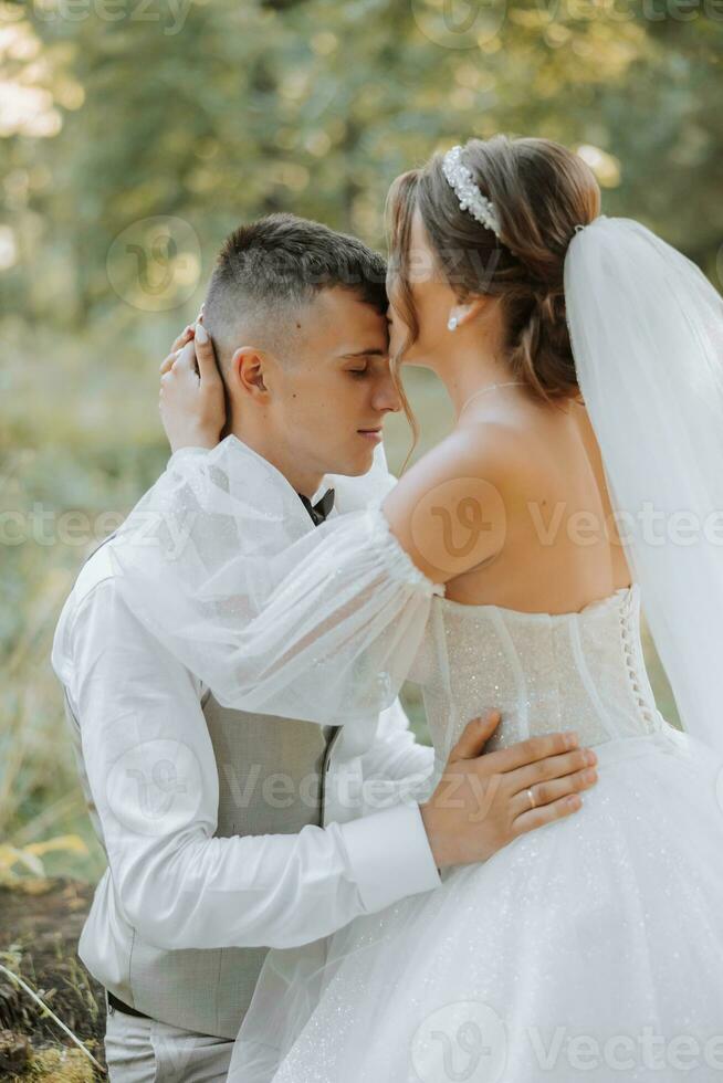 Portrait of a beautiful couple in love on your wedding day. A walk in the park in the sunlight. Amazing kisses and hugs of the bride and groom with a bouquet photo