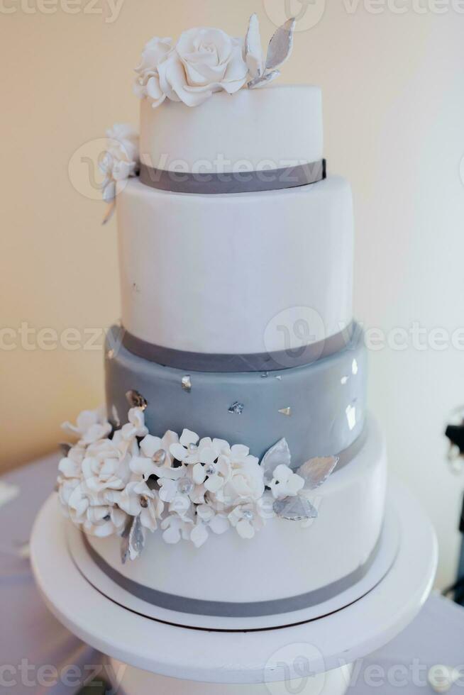 royal wedding three-tier cake, in white and gray colors, decorated with white flowers on a white stand. Royal wedding, sweets photo