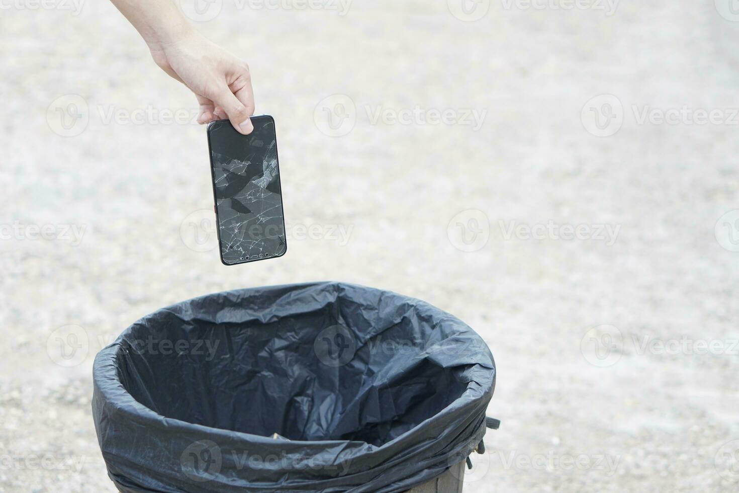 Closeup hand throw broken smartphone into the bin.Concept, hazardous electronic waste should sort before throwing for safety with environment. Technological garbage management. photo