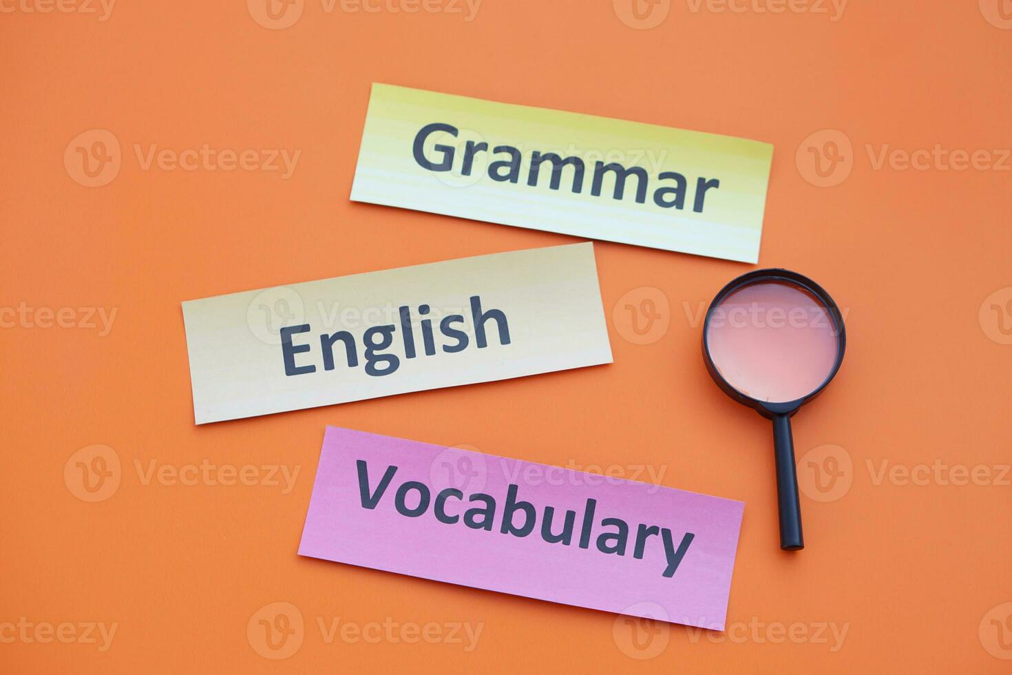 Paper word cards with text Vocabulary, English, Grammar. Magnifying glass. Orange background. Concept. Education material. Teaching aid. Learning language. photo
