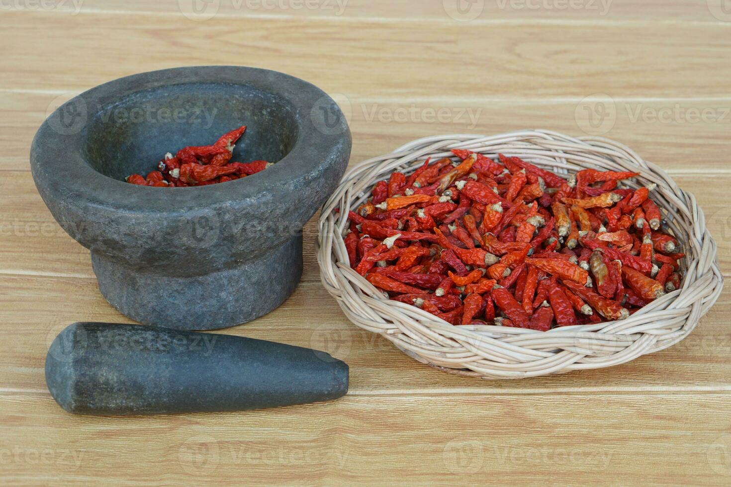 Old granite stone mortar with pestle and basket of red dried chillies for cooking.Concept, kitchen utensils .Thai cooking tool, use to pound chili paste or curry paste. photo