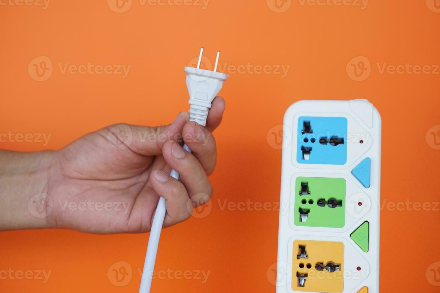 Close up hands hold electric power plug and pulling out from portable socket. isolated on orange background. Concept, save electricity power.Campaign to plug off after finish using electric appliance photo