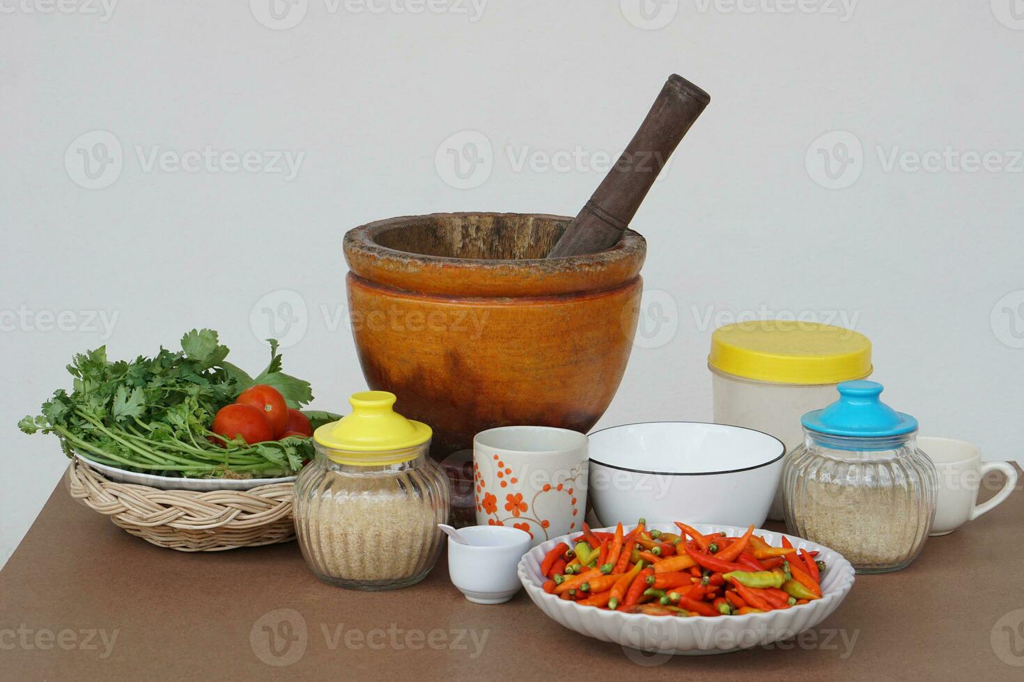 Wooden mortar,pestle, vegetables, plate of red chillies, glass jar of sugar, ceramic bowls and mugs. Concept,preparing food ingredient and equipment for cooking. Thai traditional cooking style. photo