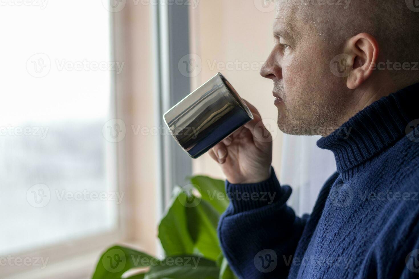Portrait of the mid aged man with grey hair, wearing warm, dark blue sweater, drinking coffee. People photo