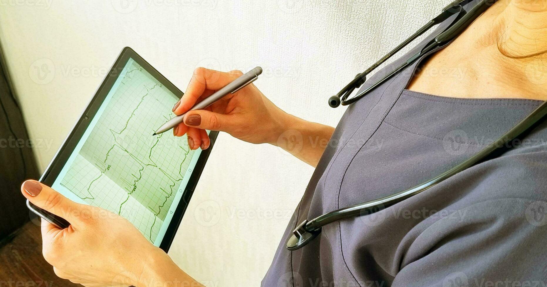 Shot of the female doctor in uniform against the white wall studying cardiogram on the tablet. Healthcare photo