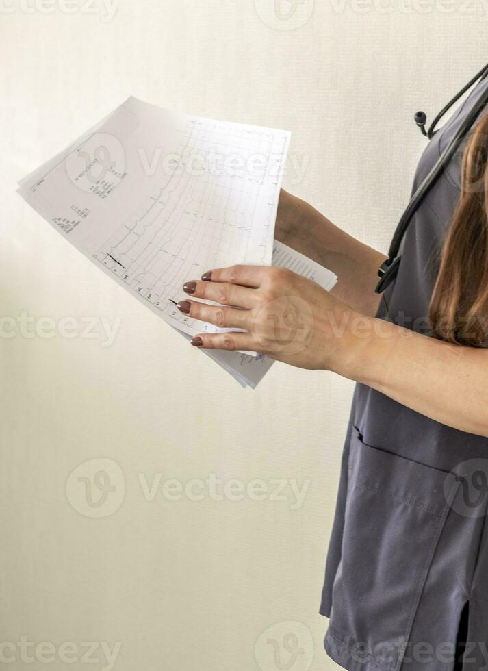 Shot of the female doctor in uniform against the white wall studying cardiogram. Healthcare photo