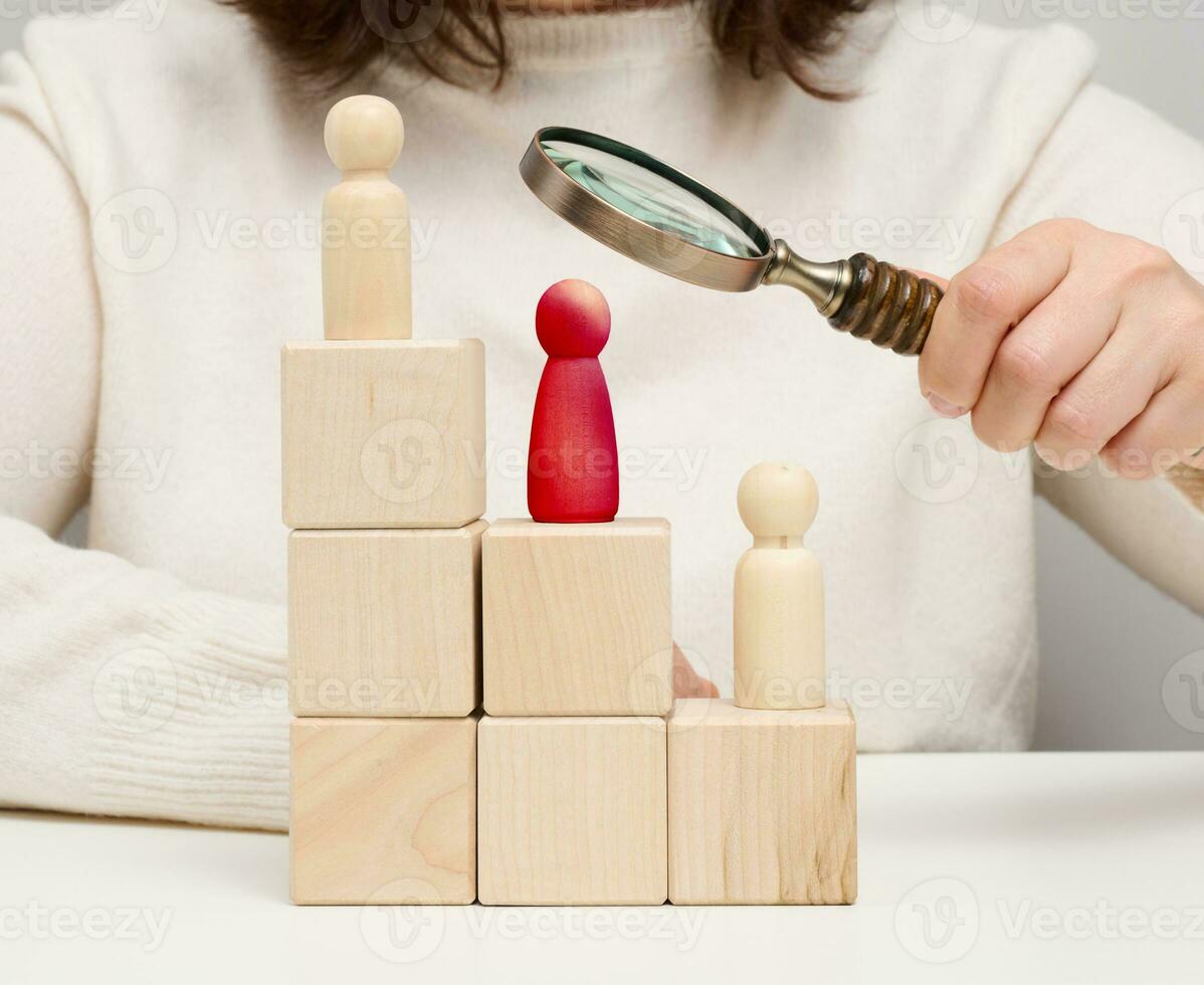 Woman holding a magnifying glass and wooden men on a white table. Personnel recruitment concept, talented employees. photo