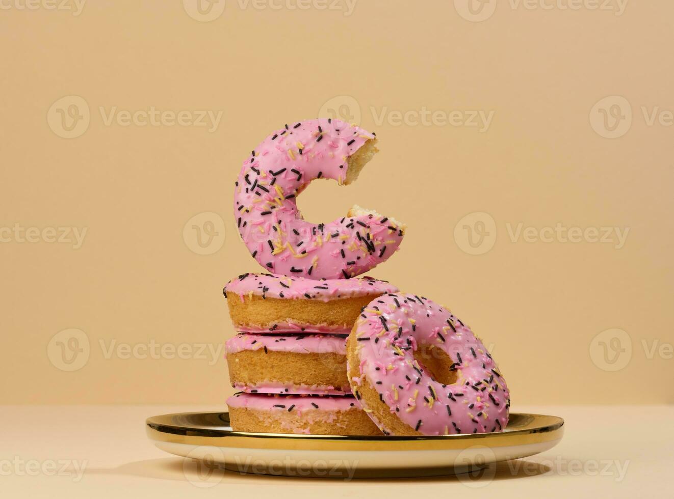 Donut covered with pink glaze and sprinkled with colorful sprinkles on a round plate photo