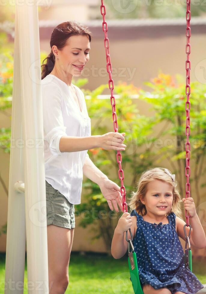 Mom rocks her daughter on a swing photo