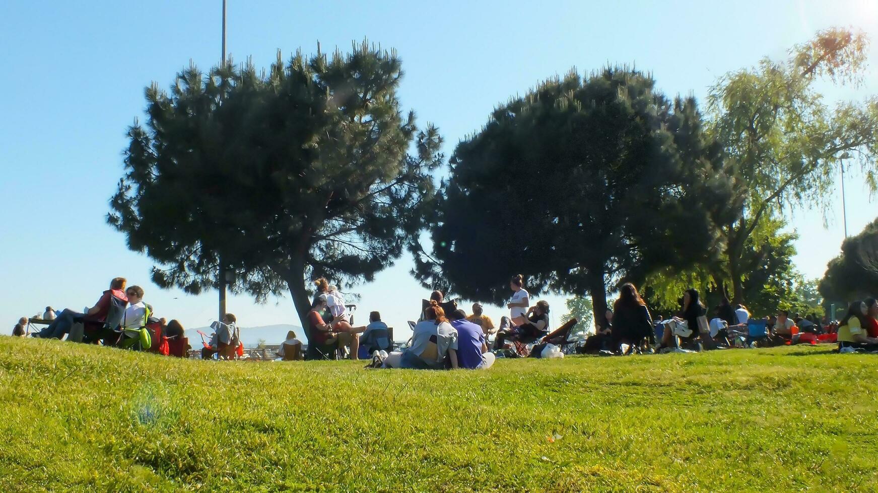 People picnic on the grass by the sea. Group of people sitting on folding chairs on the grass at the weekend. Selective focus, noise and grain included. Suadiye, Istanbul, Turkey - May 21, 2022. photo