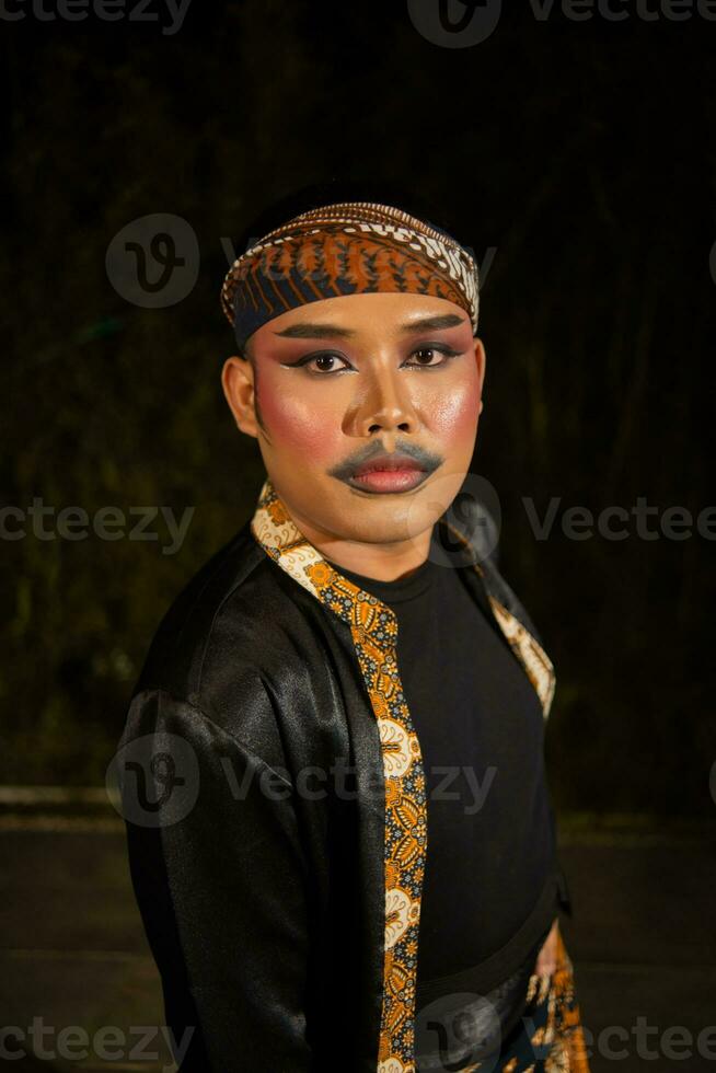 a male dancer wearing a black costume full of batik patterns with make-up on his face photo