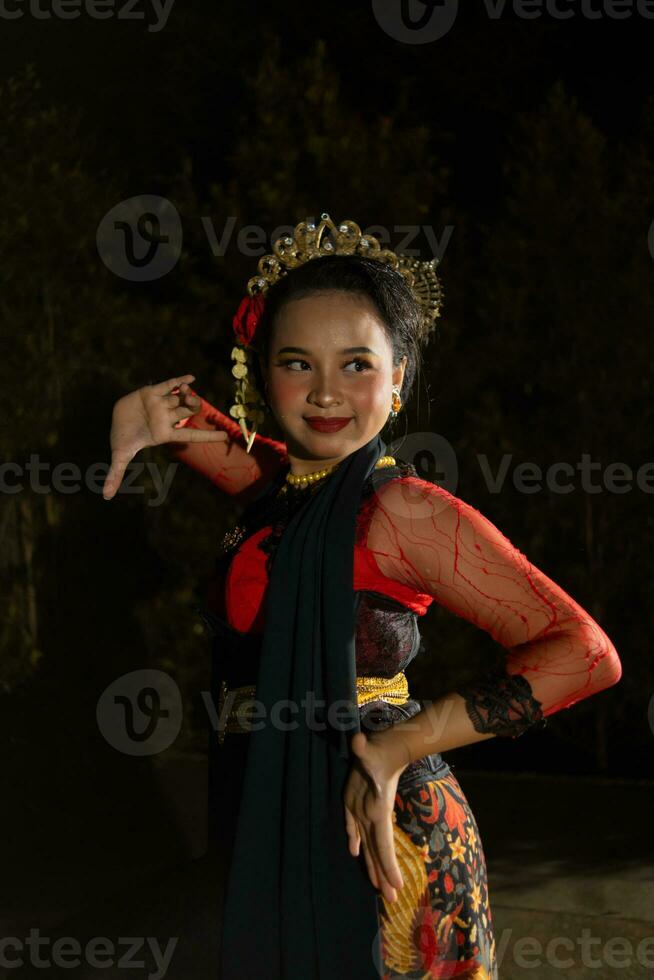 a Javanese dancer wearing a black shawl and jasmine on her head while dancing on stage at night photo