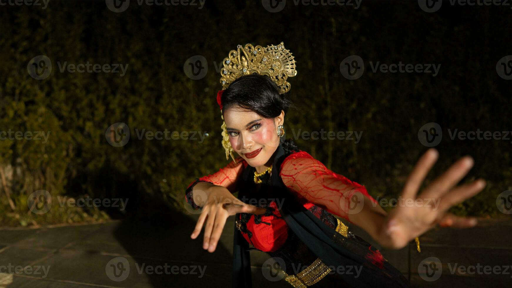 a Balinese dancer dances under the stage lights which highlight her red dress and create an elegant visual photo