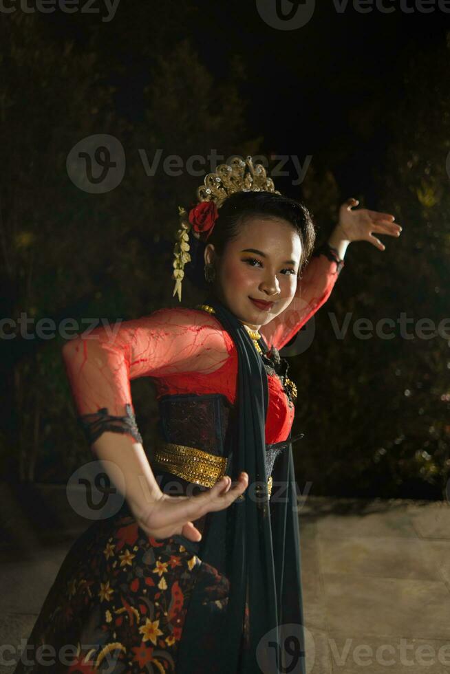 a Javanese dancer wearing a black shawl and jasmine on her head while dancing on stage at night photo