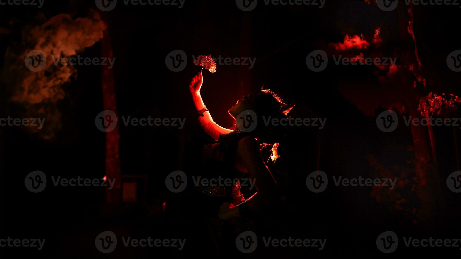 the silhouette of a female dancer holding sparkling jewelry and looking sharp in the dark with fire burning in the background photo