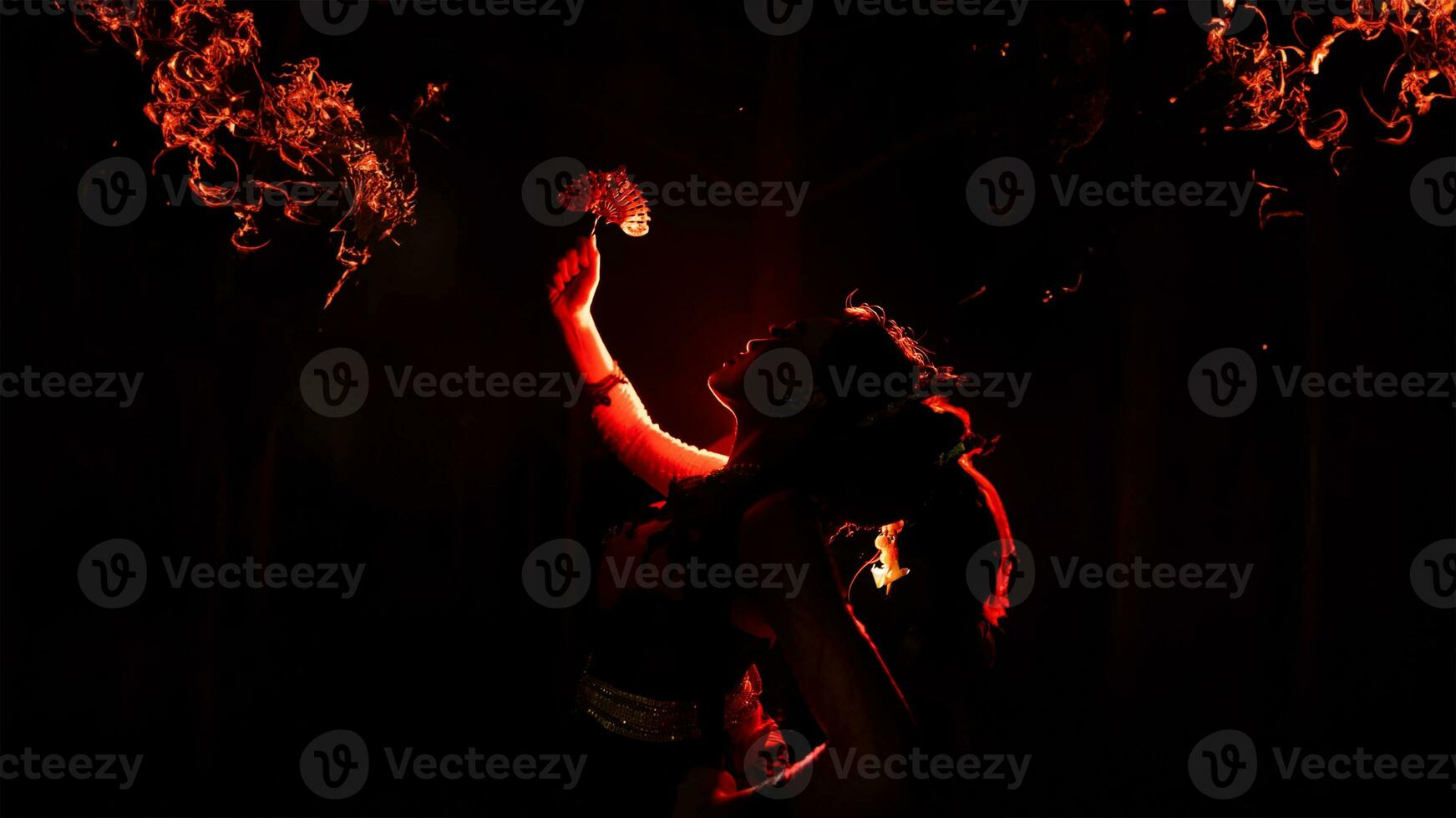 the silhouette of a female dancer holding sparkling jewelry and looking sharp in the dark with fire burning in the background photo