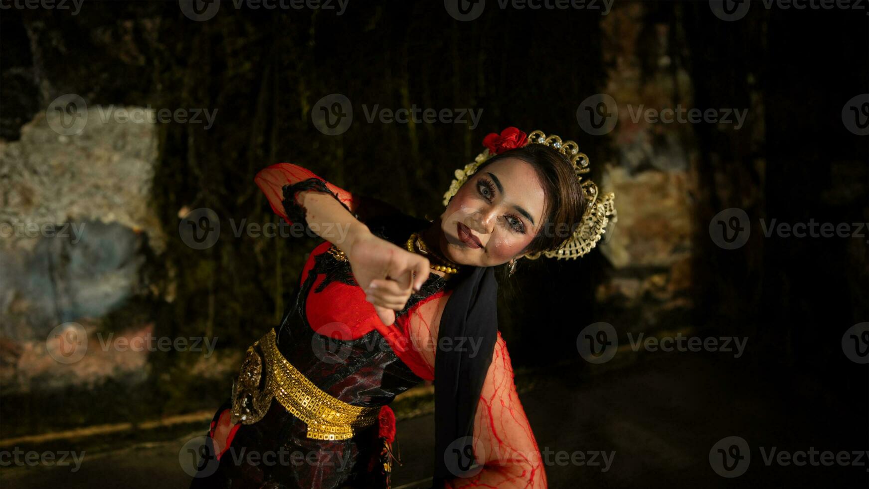 a Balinese dancer dances under the stage lights which highlight her red dress and create an elegant visual photo