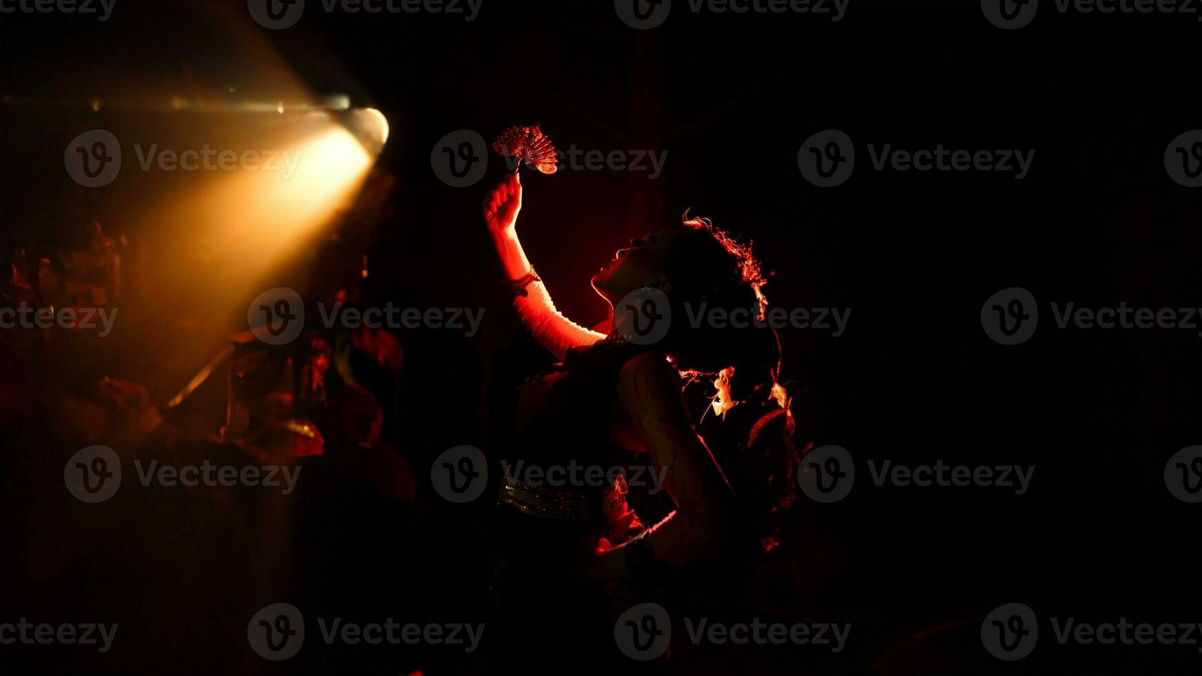 The silhouette of a female dancer holding jewelry in the dark of night is lit by the light of a burning fire photo