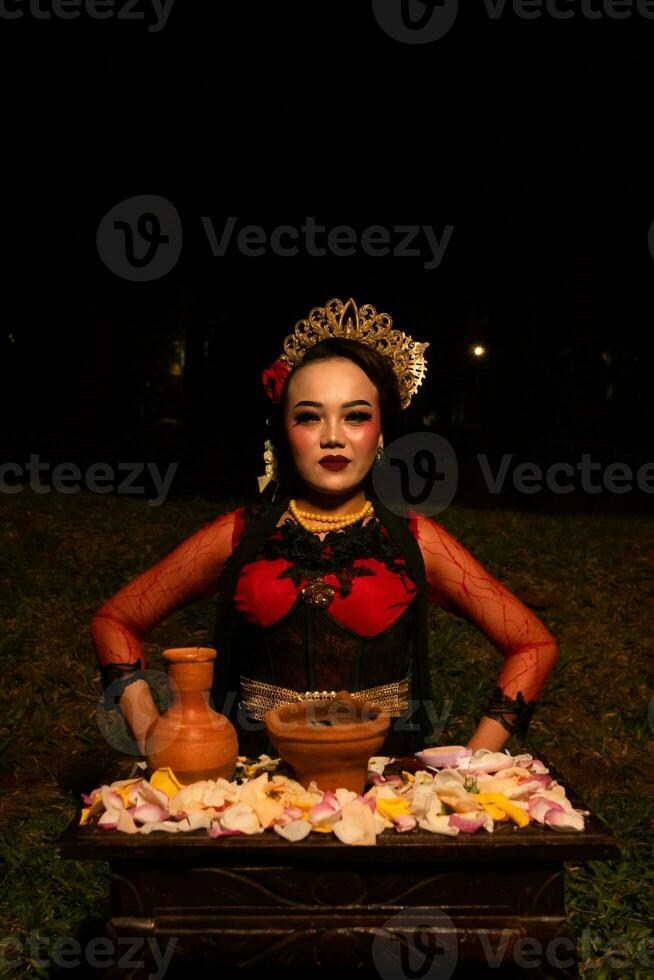 Close up shot of an Asian girl in red clothes sitting on her knees in front of a flower offering photo