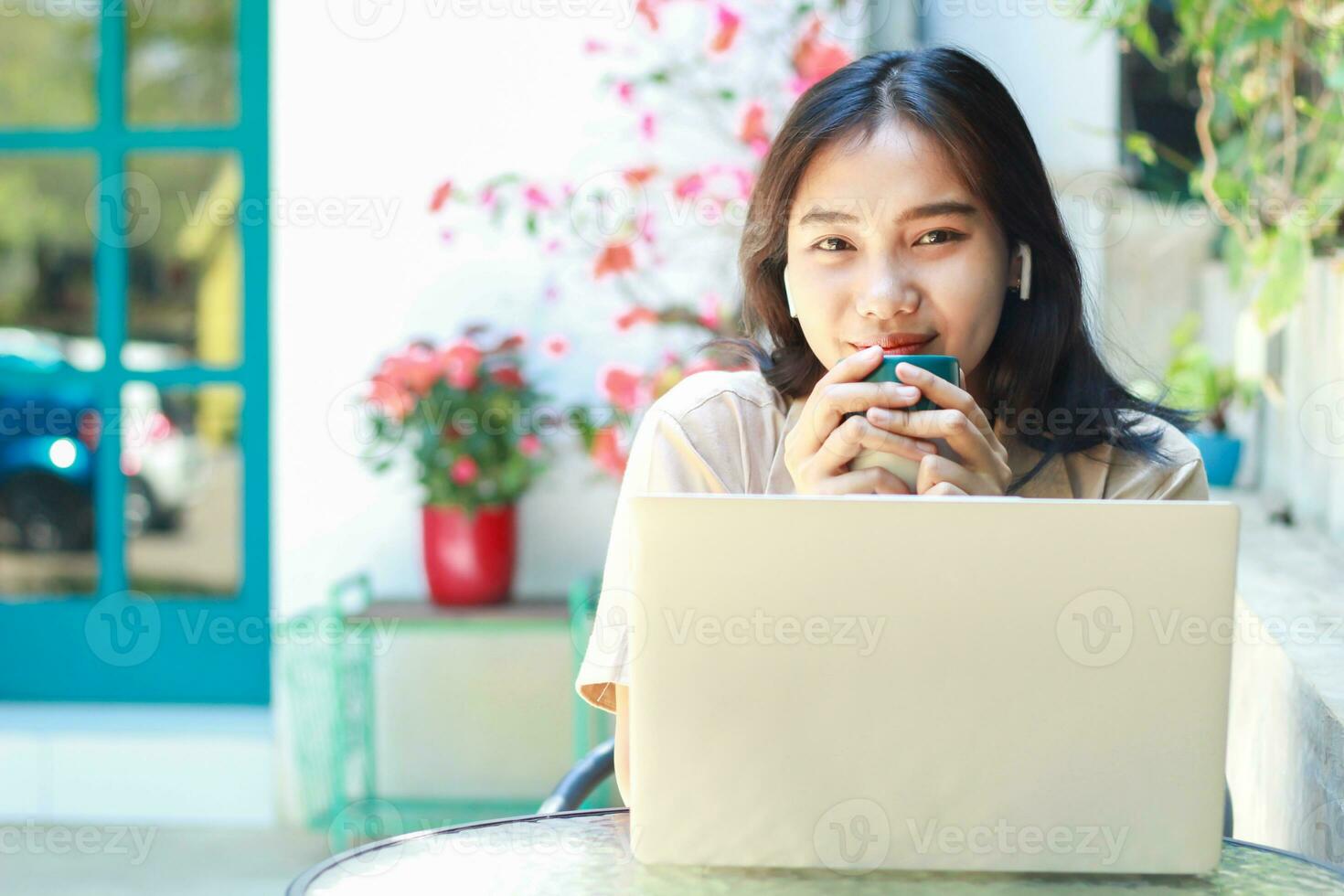 happy asian woman drink coffe while work in cafe with laptop sit in outdoors wearing casual clothes fashionable, female remote worker smiling look at camera photo
