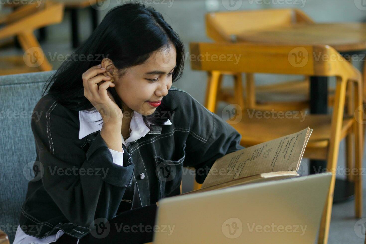 happy asian woman reading notebook and using laptop in library to studying photo