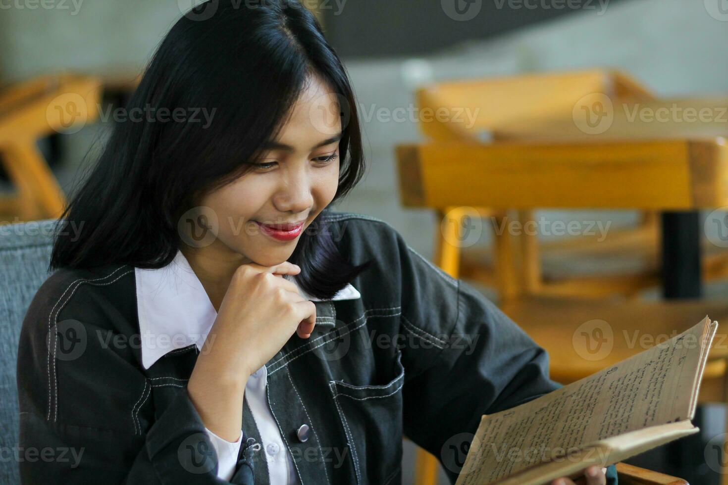 happy asian woman reading notebook and using laptop in library to studying photo