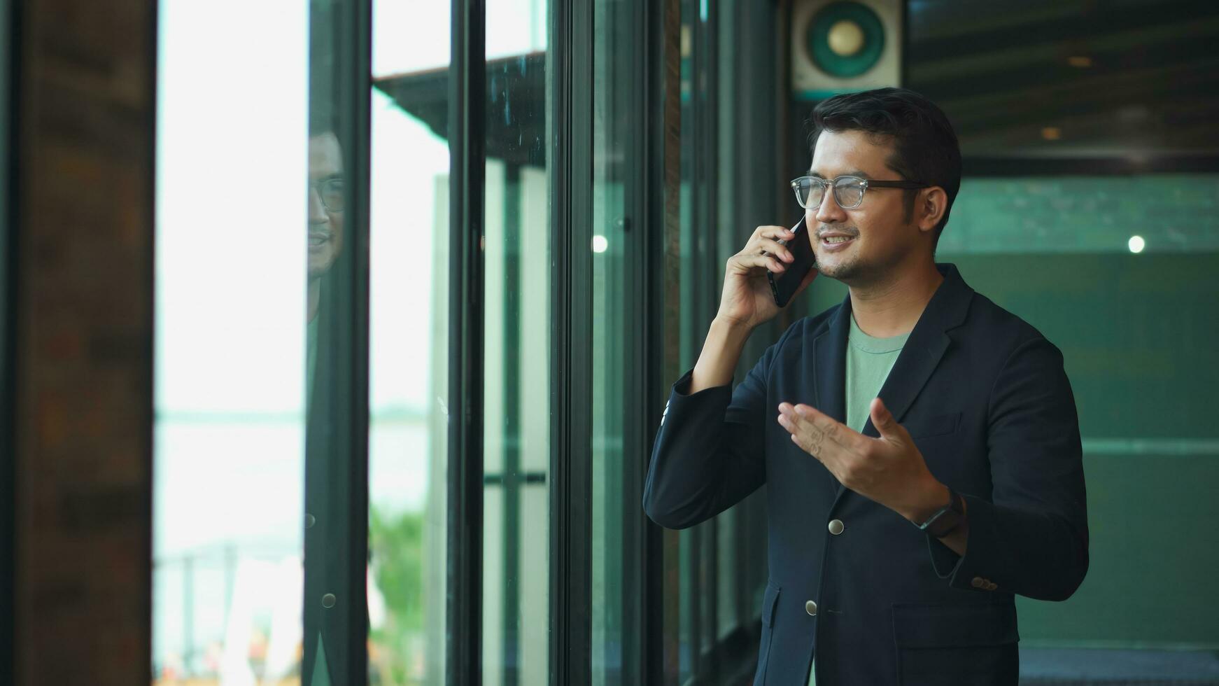 asiático negocio hombre hablando en el teléfono en el oficina, asiático trabajando a el ventana . foto