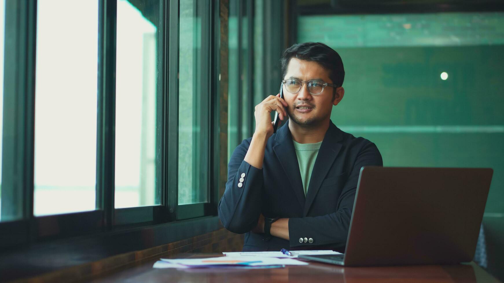 Young asian man talking phone and work from cafe with laptop computer. photo