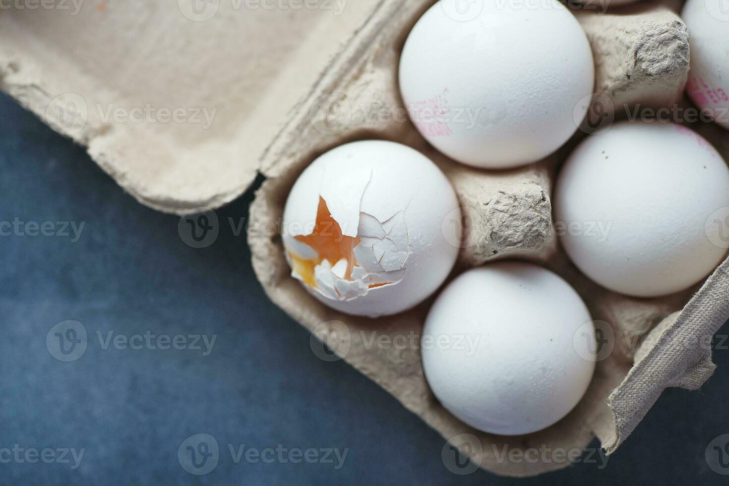 one broken egg with yellow yolk stored in carton container photo