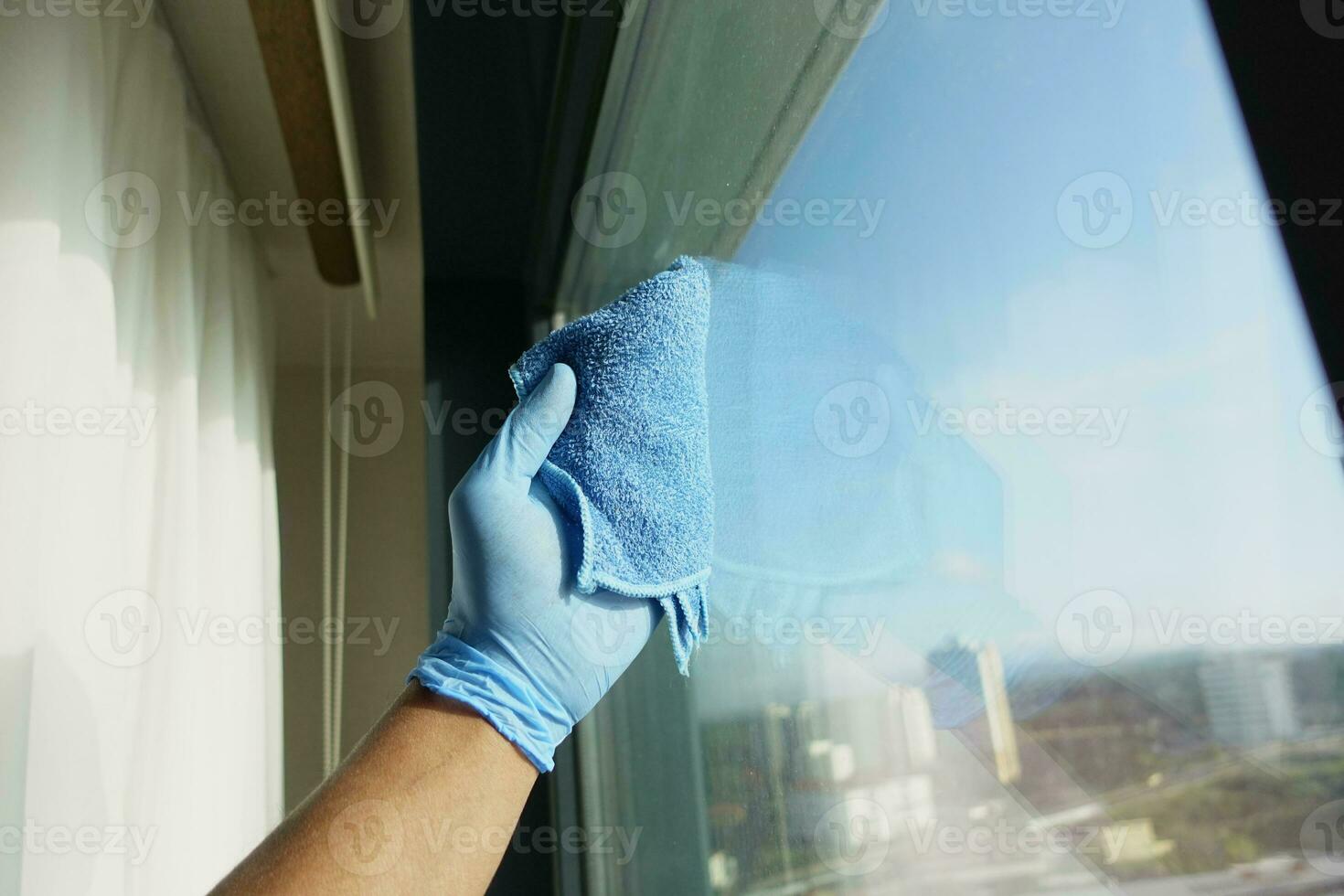 hand in blue glove cleaning window with blue rag photo