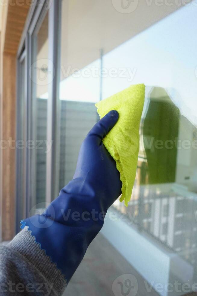 hand in blue glove cleaning window with green rag photo