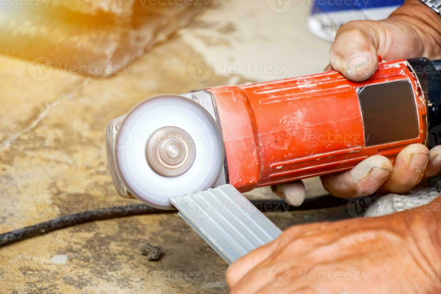 Closeup hands of laborer holding electric angle grinder working chamfer at construction site with sun flare background. photo