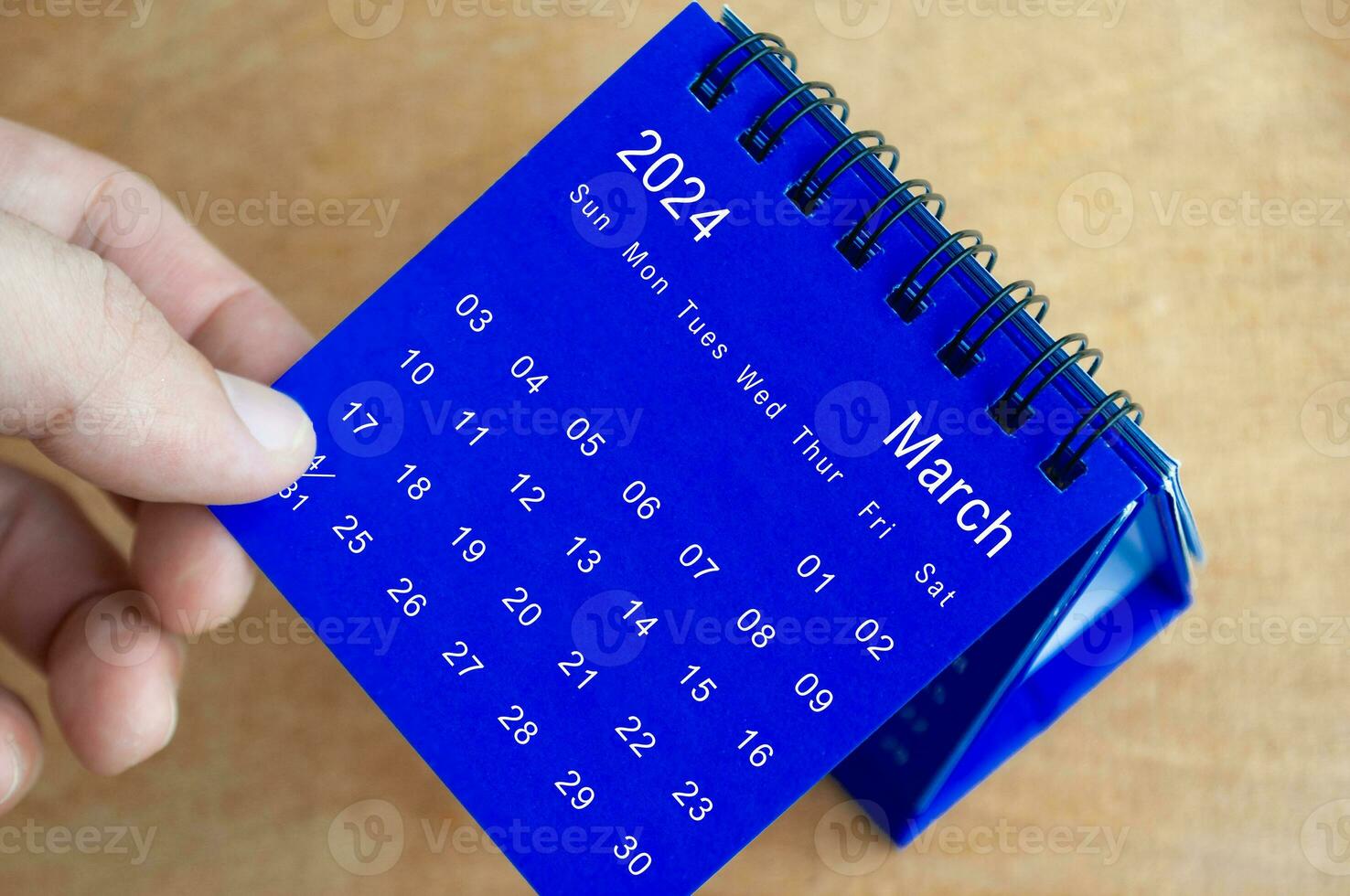 Hand showing March 2024 table calendar on wooden background. Calendar and new month concept. photo