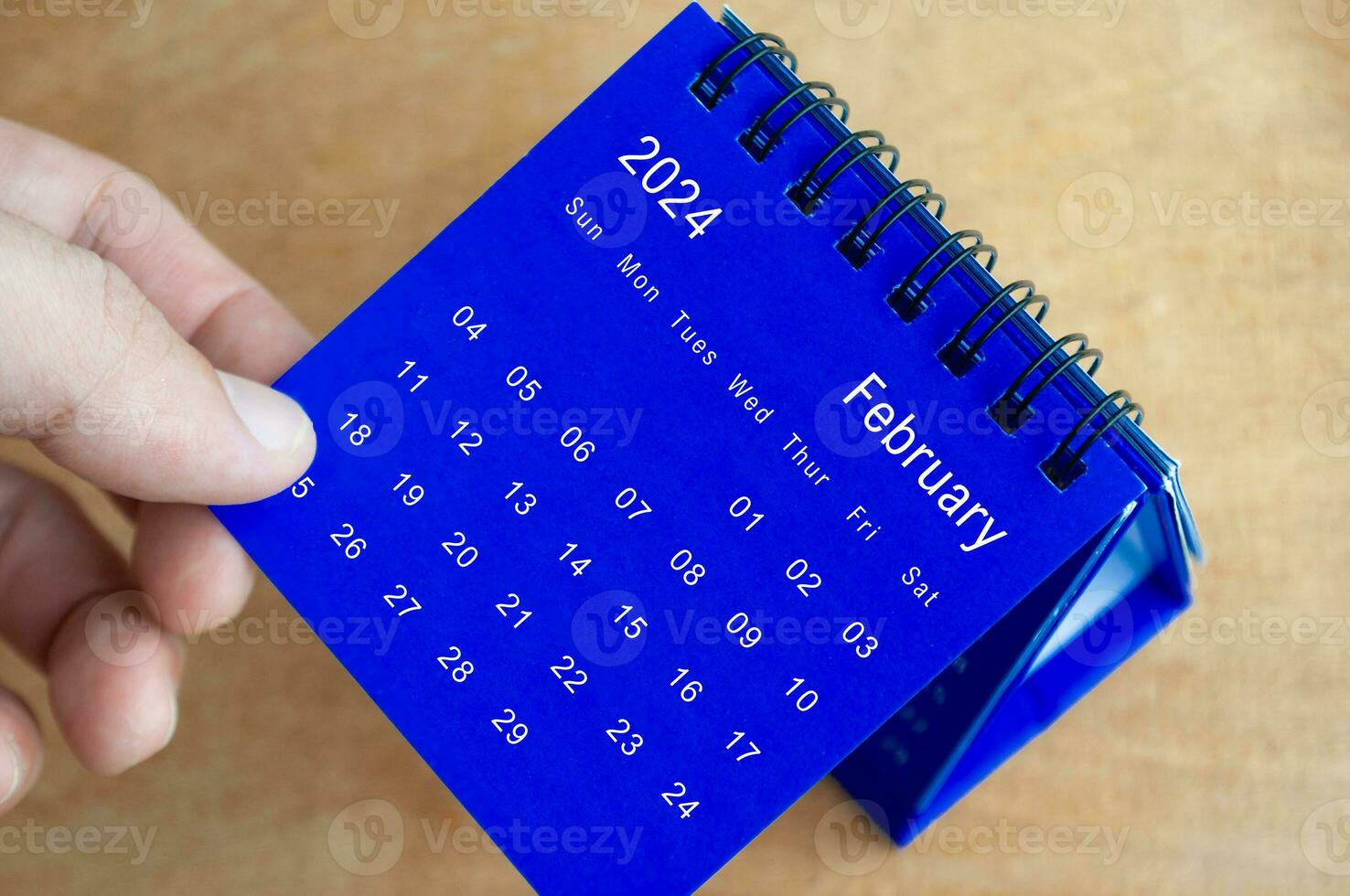 Hand showing February 2024 table calendar on wooden background. Calendar and new month concept. photo