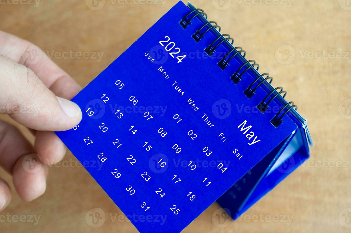 Hand showing May 2024 table calendar on wooden background. Calendar and