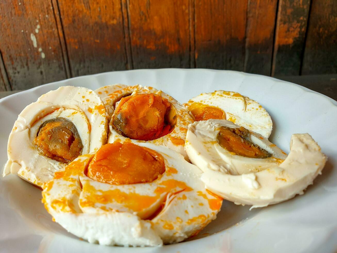 Closeup Chinese salt eggs cut in half and ready to eat on white ceramic plate on wooden background. photo